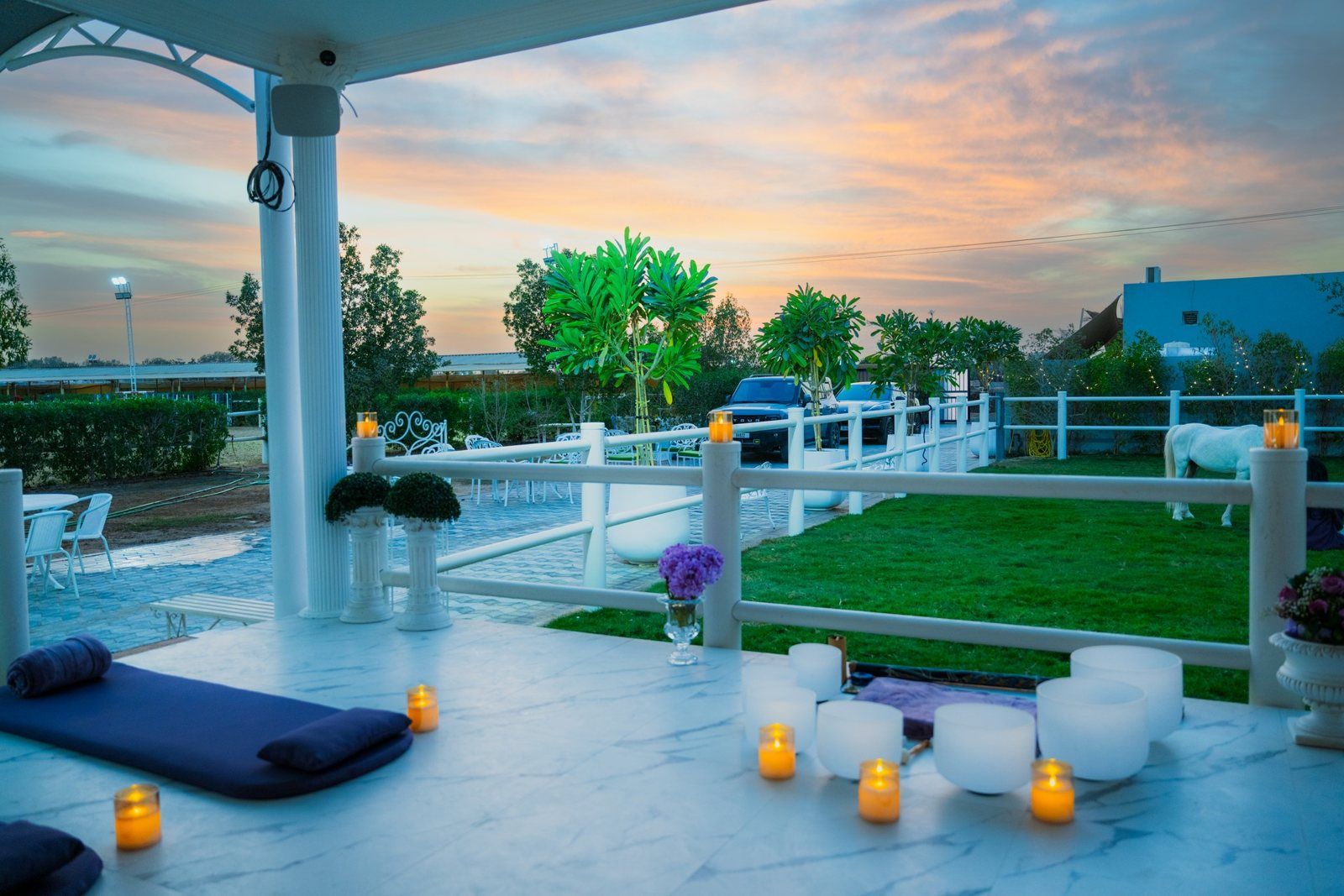 Mats, bolsters, crystal singing bowls and candles set out on the terrace at Crystalline Equine, with the paddock and a horse behind, at sunset